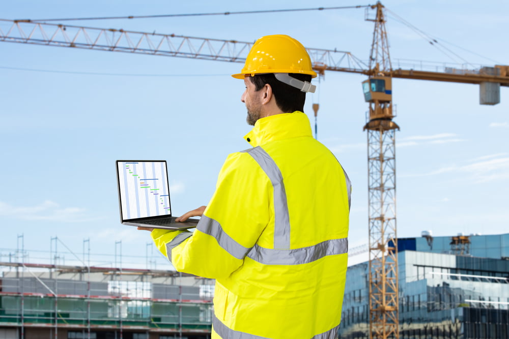 An engineer in a helmet works at a construction site, monitoring on-site asset usage with iot connected devices and technology