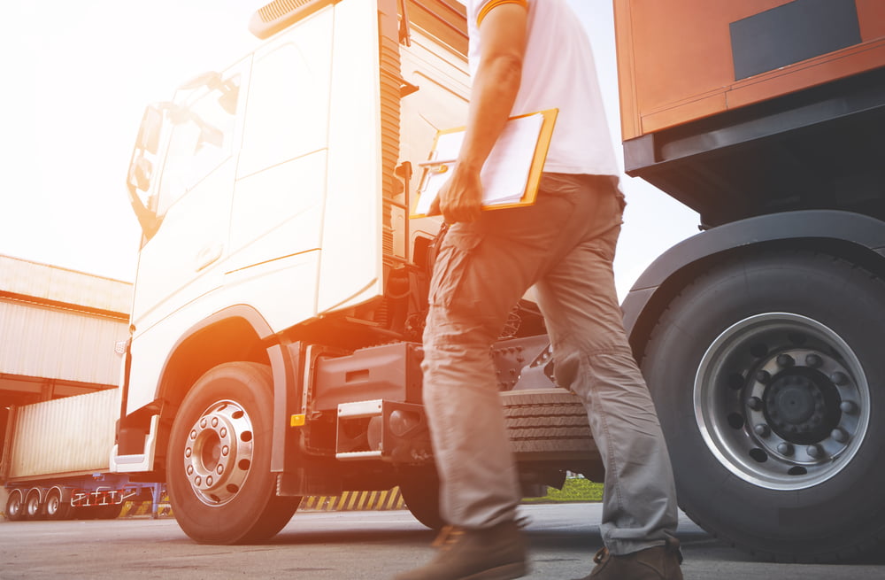 A man stands with a clipboard in hand beside a truck outside a warehouse