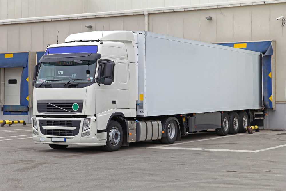 A refrigerated semitrailer is parked at a warehouse loading bay dock