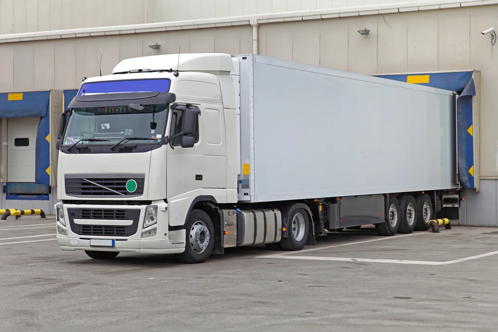 A refrigerated semitrailer is parked at a warehouse loading bay dock