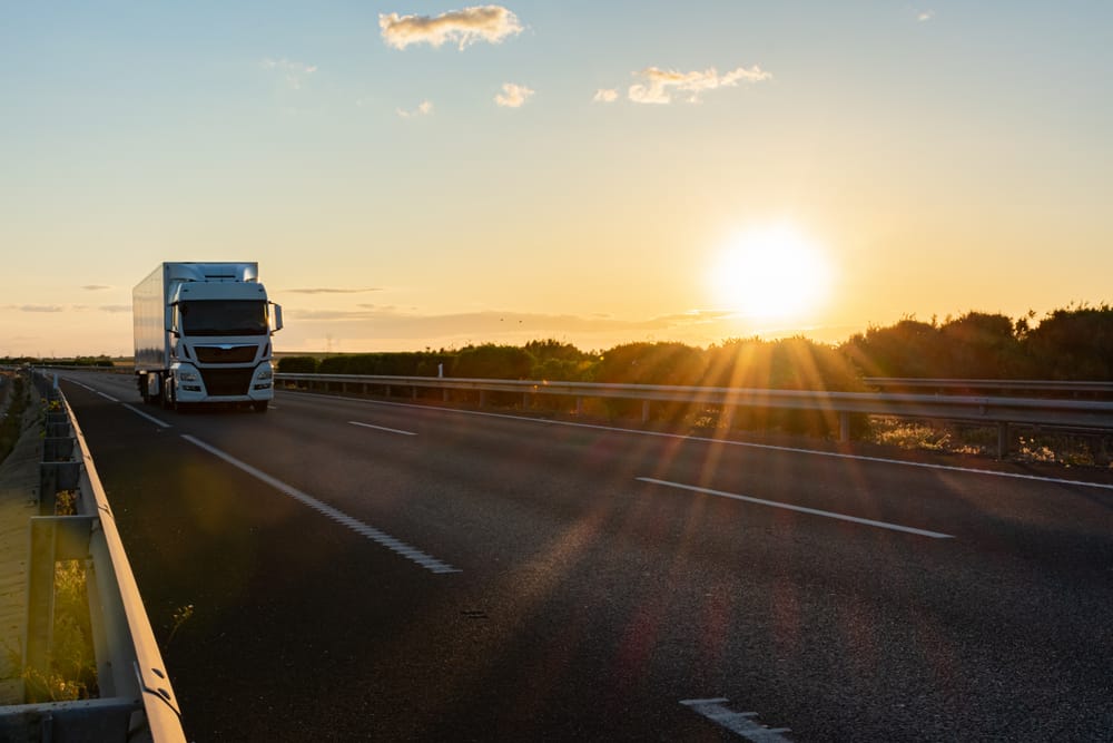 A refrigerated truck using cold chain IoT technology travels along a highway at dusk