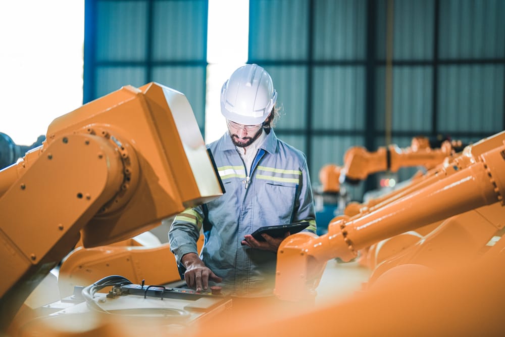 Factory engineer using a tablet to inspect robotic machinery, illustrating AI automation in industrial processes