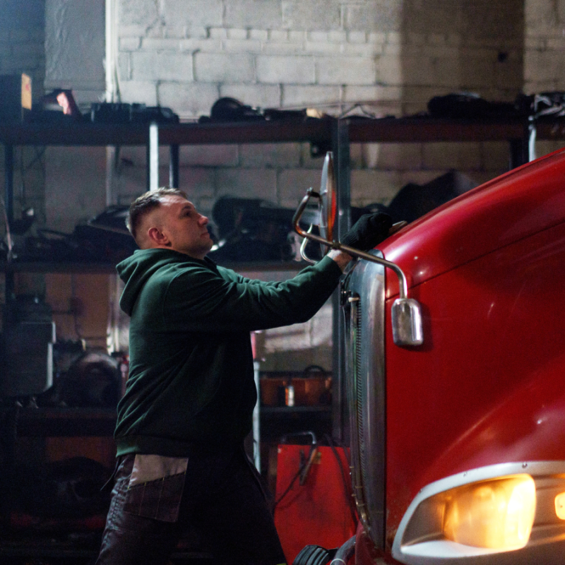 A truck driver inspects the front of his rig, representing the role of driver behavior monitoring in boosting fleet safety and performance.