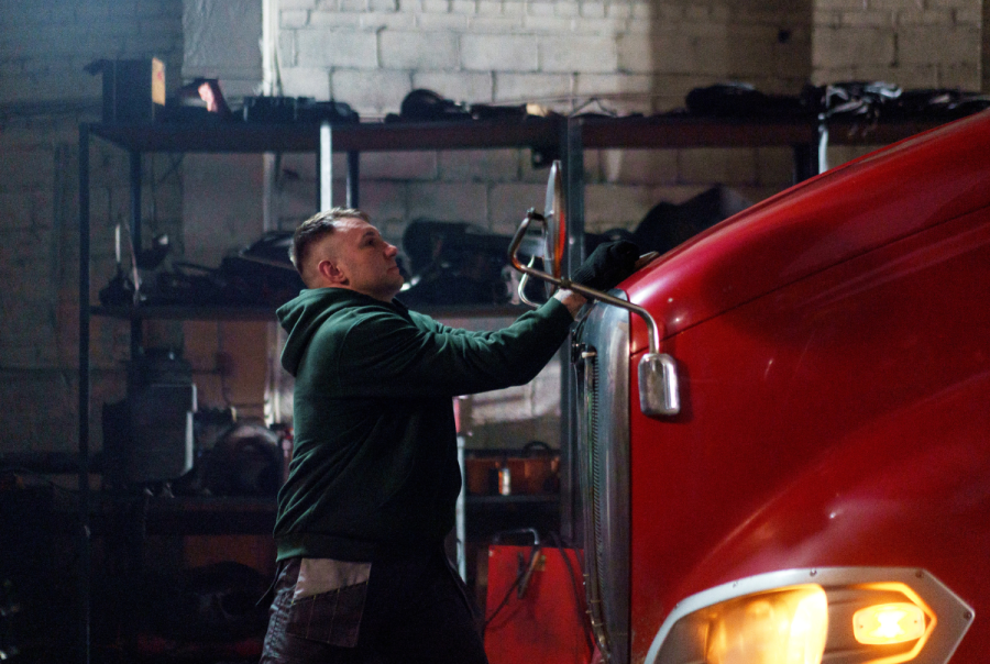 A truck driver inspects the front of his rig, representing the role of driver behavior monitoring in boosting fleet safety and performance.