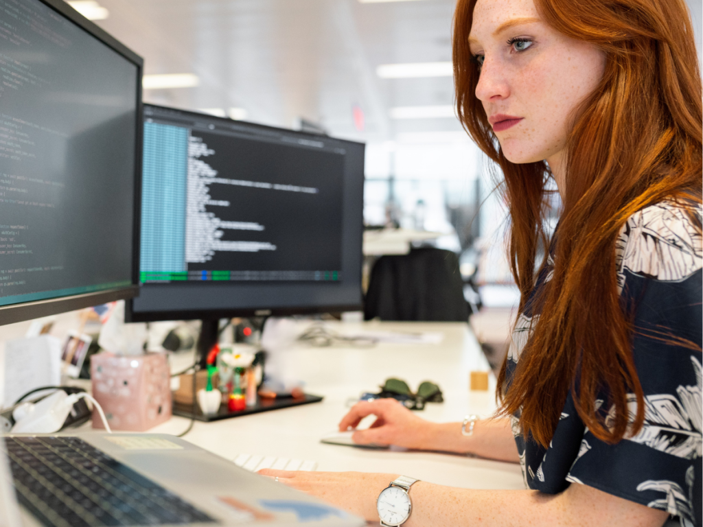 A female manager sits at her desk with multiple screens analysing data
